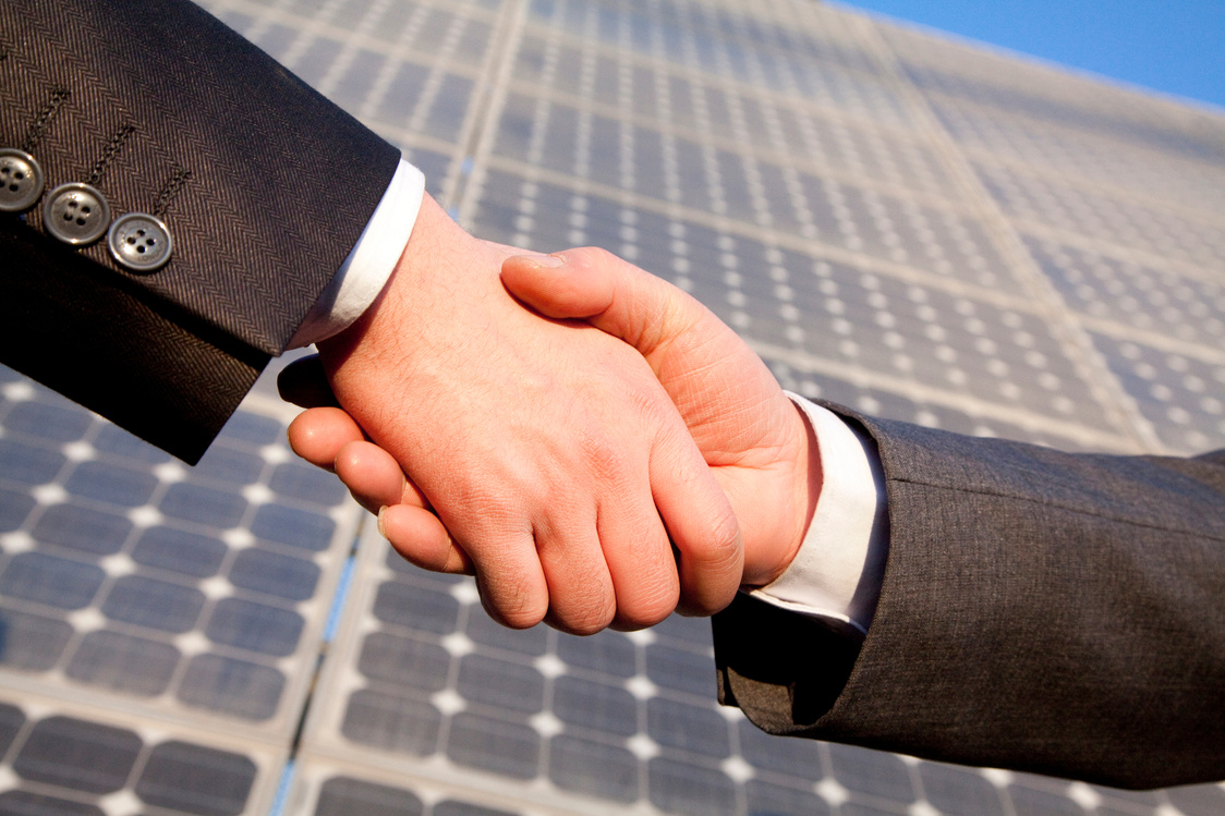 Shaking hands in front of solar panels